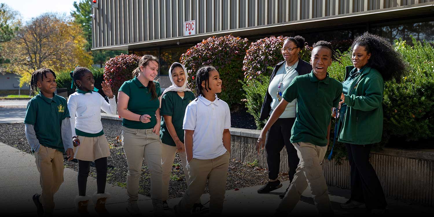 Smiling students and school leaders walking outside of the school